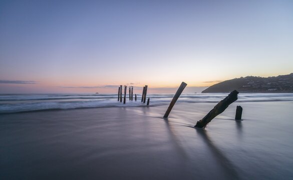 Old broken bridge, posts in the water on the beach at dusk, St. Clair, Dunedin, Southland, New Zealand