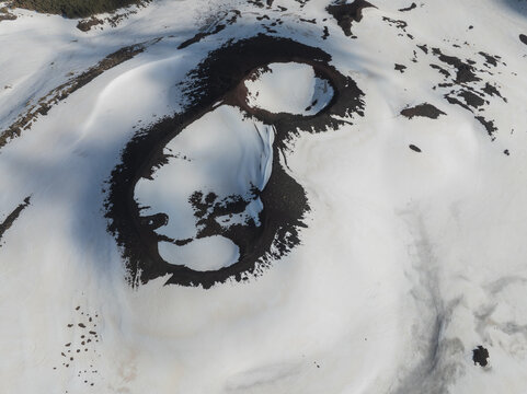 Aerial view of the snow-covered volcanic craters on the Versante sud dell' Etna with dark lava rock and shadows Nicolosi, Sicilia, Italy.