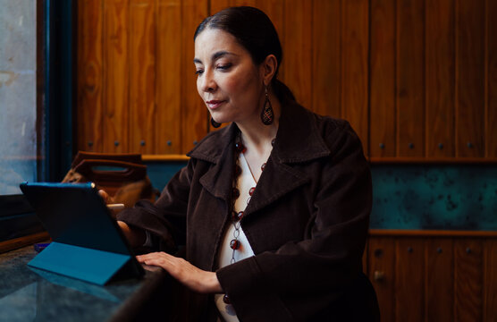 Hispanic woman smiling with direct gaze while holding stylus and tablet, illustrating friendly confidence, tech fluency, and approachable professionalism in a mobile workspace.