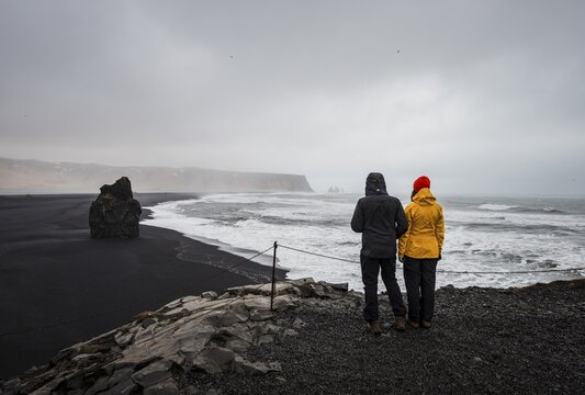 Two tourists overlooking a black sandy beach, bad weather, Reynisfjara Beach, South Iceland, Iceland