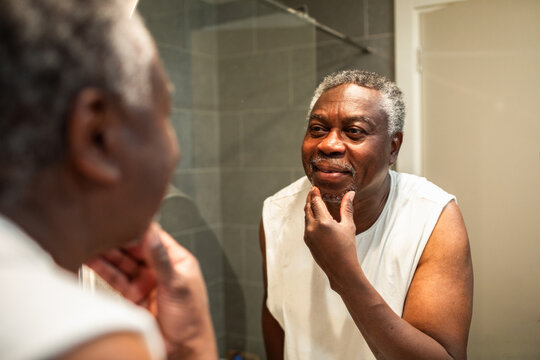 Senior man checking face in bathroom mirror at home