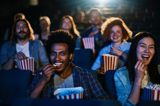 Friends laughing and eating popcorn at movie theater