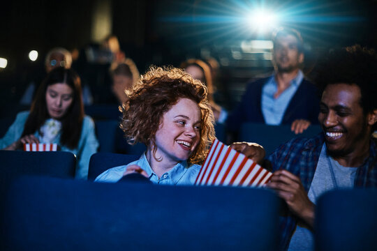 Friends laughing and sharing popcorn at movie theater