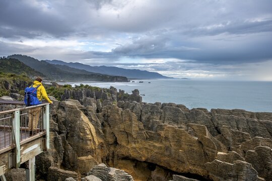 Young man on viewing platform looking over coastal landscape with sandstone rocks, Pancake Rocks, Paparoa National Park, Punakaiki, West Coast, South Island, New Zealand