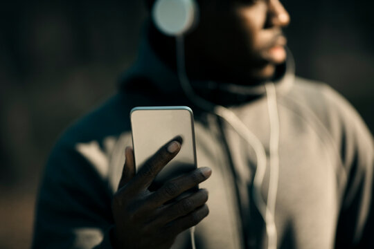 Man in hoodie with headphones using smartphone outdoors