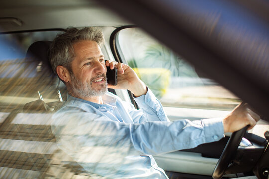 Mature man talking on smartphone while driving car