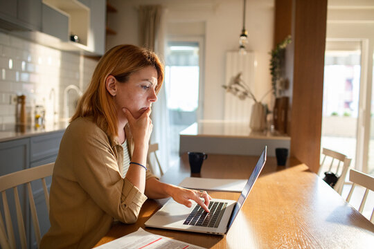 Woman working on laptop at home kitchen table