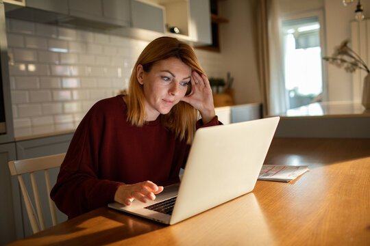 Woman paying bills on laptop at home kitchen