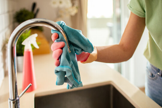 Gloved hand cleaning kitchen faucet at home