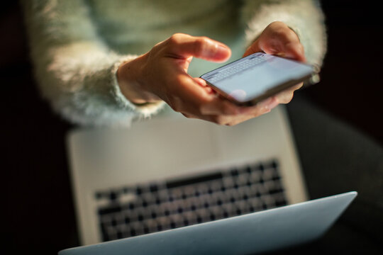 Person texting on smartphone over laptop at home
