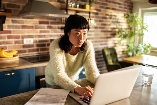 Focused woman paying bills on laptop in home kitchen