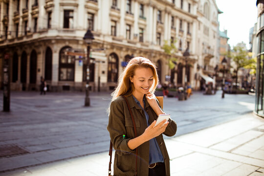 Smiling woman using smartphone on sunny european city street