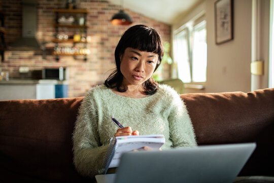 Woman taking notes while working on laptop in cozy living room