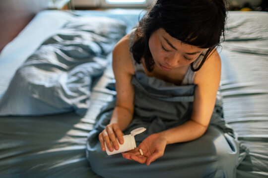 Young woman taking pills in bed at home