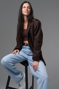 Stylish woman posing on stool wearing brown oversized blazer and light blue jeans