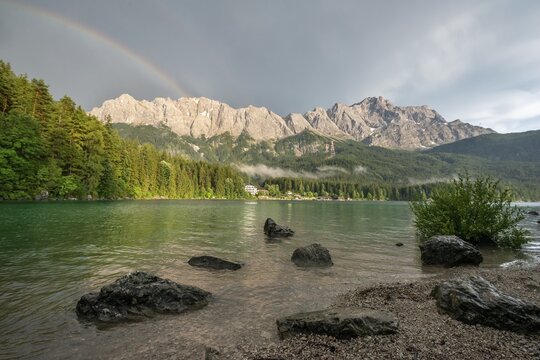 Rocks on the shore, Eibsee lake in front of Zugspitze massif with Zugspitze with rainbow, behind thunderclouds, Wetterstein range, near Grainau, Upper Bavaria, Bavaria, Germany