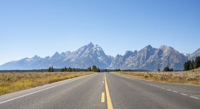 Country road through autumn landscape, rugged mountain peaks behind, Grand Teton and The Jaw, Teton Range mountain range, Grand Teton National Park, Wyoming, USA