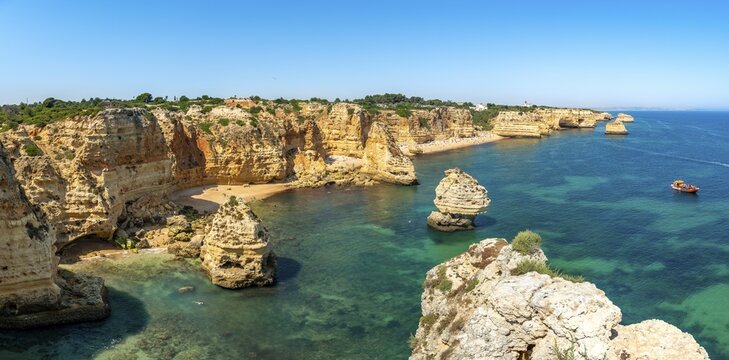 View of cliff of craggy sandstone rocks, rock formations in the turquoise sea, sandy beach on the cliff, Praia da Marinha, Algarve, Lagos, Portugal