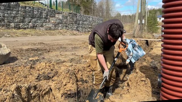 A man and his 8-year-old son dig a drainage trench together on their countryside property, working outdoors with shovels to improve land drainage and prevent water accumulation