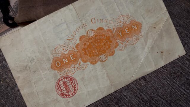 Macro video of the reverse side of an antique Japanese 1 yen Daikoku banknote, featuring ornate orange printing, decorative floral patterns, central lettering, red seal, and aged paper texture.