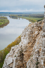 Fototapeta premium Boulder Formations Near Tranquil Water. Harsh Rocky Cliffs Adjacent To Serene Reflective Waters. Picture Of Jagged Stone Edges Beside Calm Sparkling River Under Overcast Sky