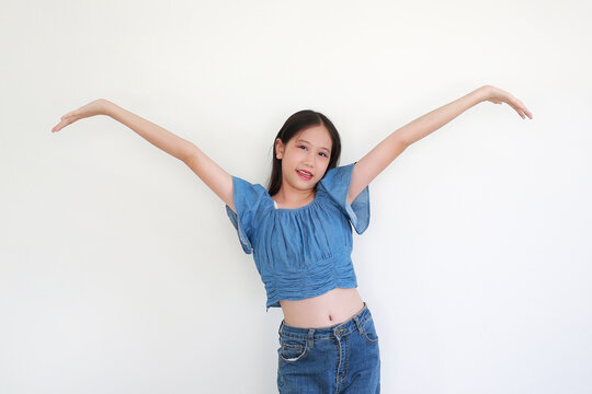 Cheerful young girl in stylish blue denim crop top and jeans posing with her arms wide open against white background.