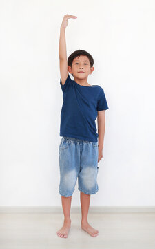 Portrait of young Asian boy raising his hand to check his height against white wall room.