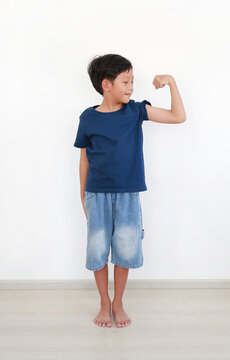 Asian young boy age 8-9 years old showing off his arm muscle while standing on white room background. Full body.