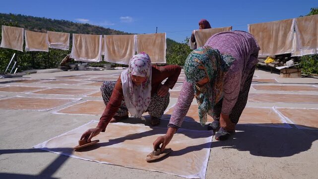 Women spread grape pestil on cloth sheets under the sun on a rural rooftop, showing traditional Anatolian food production, handmade harvest work, local culinary heritage, and authentic teamwork today.
