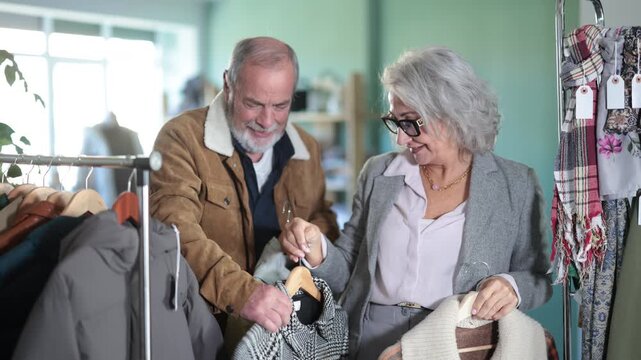 Mature husband and wife choose coats and jackets together, they discuss the style and size. Buyers of pensioners came to buy outerwear 
