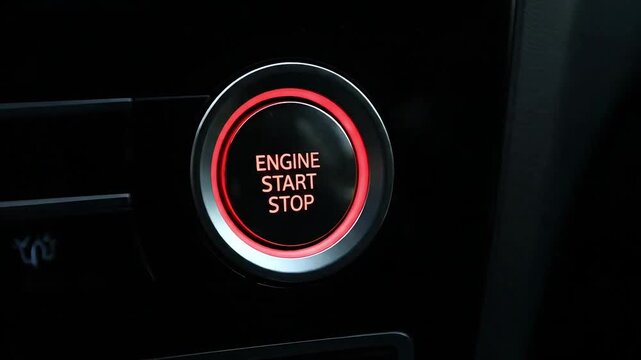 Close up of a human finger pressing modern car engine start stop button with illuminated red