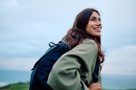 Young woman smiling, looking away while hiking outdoors, enjoying the fresh air and scenic view with a backpack
