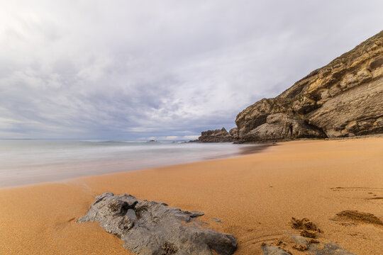 A calm and deserted Tagle (Sable) beach with fine-grained golden sand under a moody overcast sky, capturing a natural atmosphere. Tagle, Suances, Cantabria, Spain.