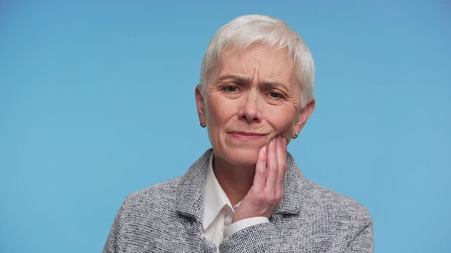 Mature woman suffering from tooth pain on blue background