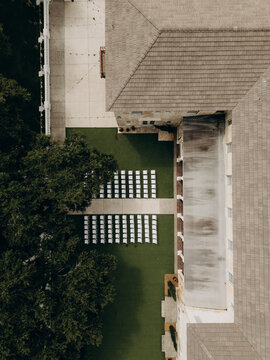 An aerial shot of a wedding venue with neatly arranged rows of white chairs on a green lawn next to the building. 