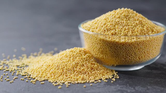 millet grains in a glass plate and scattered on a dark kitchen table. organic millet in a clear glass bowl on a black marble background.