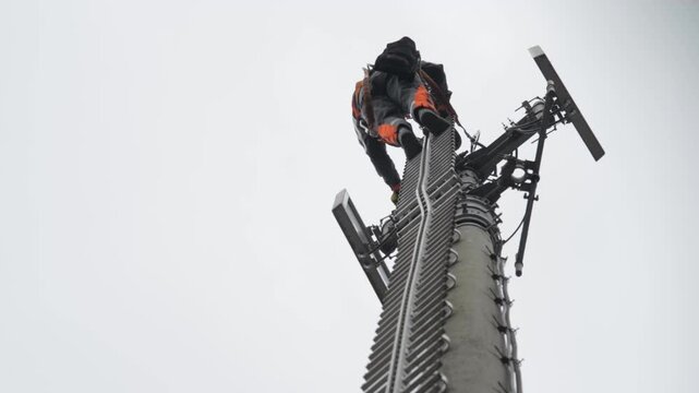 Telecommunications Worker Climbing Tower for Maintenance Against Cloudy Sky
