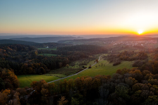 Aerial view of the Heuberger Tor area with rolling hills, autumn forests, and a winding road under a golden sunset in Tubingen, Baden-Wurttemberg, Germany.