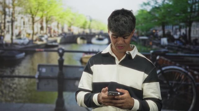 Man holding smartphone, scrolling with both hands while looking down on a street; contemplative solitude.