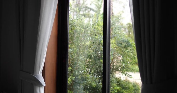 Cinematic view of heavy rain falling outside a window with raindrops on glass, cozy home atmosphere with curtains, rainy day aesthetic