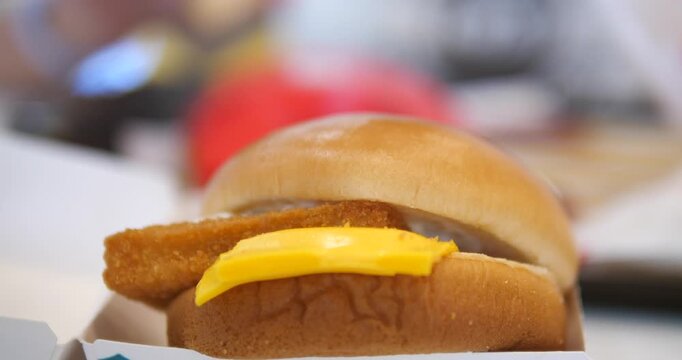 Close-up cinematic shot of a delicious crispy fish burger with melted yellow cheese on a soft bun, fast food and appetizing meal concept