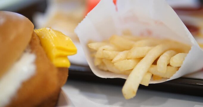 Close-up cinematic shot of a crispy fish burger with creamy tartar sauce and yellow cheese, appetizing fast food meal with fries background