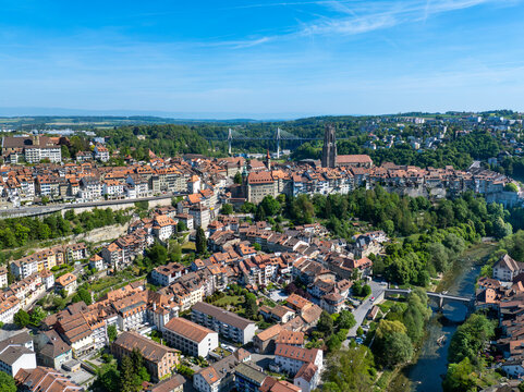 Aerial view of St-Nicolas Cathedral and the historic old town with red-tiled rooftops, the Sarine river, and the Poya Bridge under a clear blue sky in Fribourg, Fribourg, Switzerland.