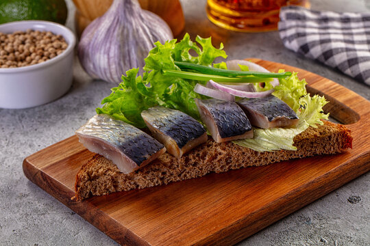 Salted herring appetizer on dark rye bread with lettuce and onions on a wooden board