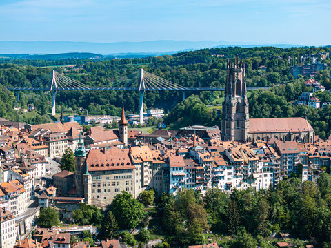 Aerial view of St-Nicolas Cathedral and the historic old town with red rooftops and the modern Poya Bridge spanning the valley in Fribourg, Fribourg, Switzerland.