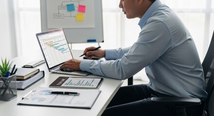 Fototapeta premium Focused professional man diligently working on a modern laptop at his office desk, managing projects and reviewing data with advanced technology in a bright, contemporary workspace