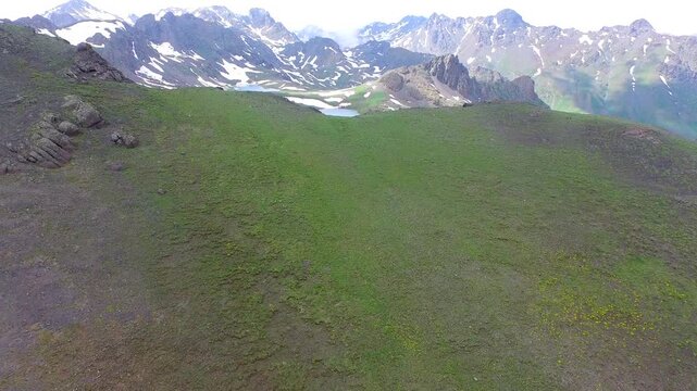 Aerial view of alpine mountain lake surrounded by melting spring snow and rugged peaks. High elevation tundra green meadow landscape create breathtaking remote wilderness scenery.