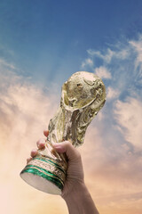 Fototapeta premium Bangkok Thailand. May 4 2026. Mock Up of the FIFA World Cup Trophy in hand and sky Background. Man holding a trophy of the FIFA World Cup in hand. Fifa 2026 winning trophy is raised up in the air.