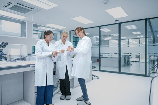 Diverse biotech research team analyzing experimental data metrics on digital tablet. Female scientists discussing strategic r&d protocols in modern laboratory.
