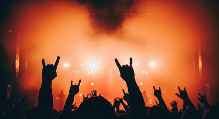 Fototapeta premium Silhouetted hands make rock gesture signs in front of a brightly lit stage with hazy atmosphere.